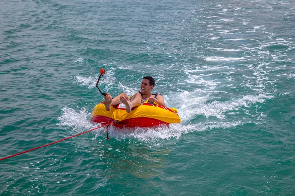 Człowiek siedzi w nadmuchiwany pierścień ciągniętym przez łódź w wodzie — Zdjęcie stockowe