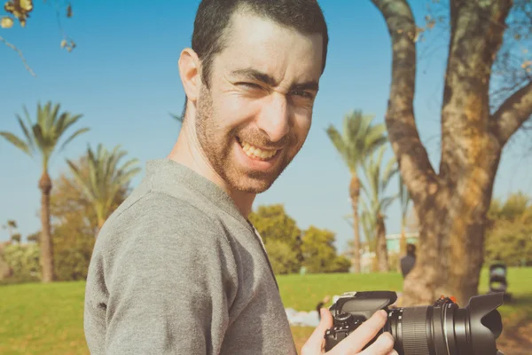 Bir dijital fotoğraf makinesi tutarak ve kameraya gülümseyen fotoğrafçı — Stok fotoğraf