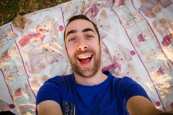 Young man lying on a sheet in the park and taking selfie picture — Stock Photo, Image