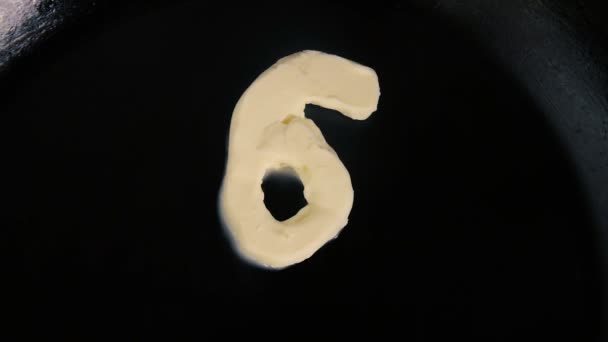 Boter in de vorm van het nummer 6 smelten op hete pan - close-up bovenaanzicht — Stockvideo