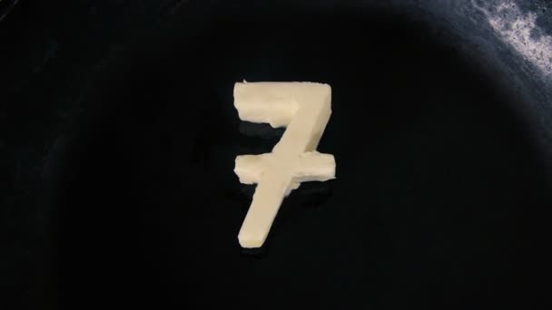 Boter in vorm van nummer 7 smelten op hete pan - close-up bovenaanzicht — Stockvideo