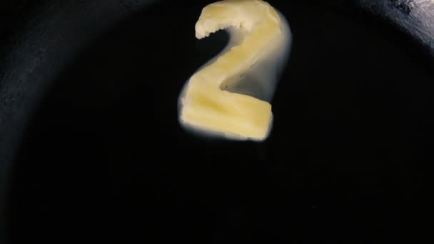 Масло у формі номеру 2 тане на гарячій сковороді крупним планом — стокове відео