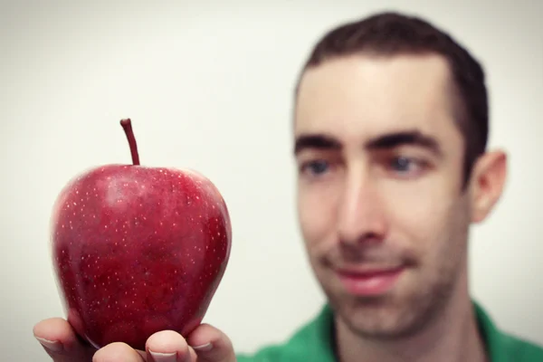 Man glimlachen en kijken naar rode appel die op zijn rechterhand geïsoleerd op wit geplaatst — Stockfoto
