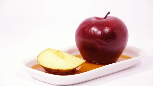 Verter miel sobre la manzana roja y la rodaja de manzana roja sobre un plato blanco con miel aislada sobre un fondo blanco — Vídeo de stock