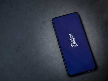 Lod, Israel - 8 Temmuz 2020: Migdal uygulama başlatma ekranı koyu mermer taşlı arka planda siyah bir cep telefonunun logosu İbranice metinde. Üst görünüm düzlüğü kopyalama alanı ile yatıyordu.