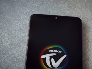 Lod, Israel - 8 Temmuz 2020: Seramik taş zemin üzerinde siyah bir cep telefonunun logosu olan Mako TV uygulaması fırlatma ekranı. Üst görünüm düzlüğü kopyalama alanı ile yatıyordu.