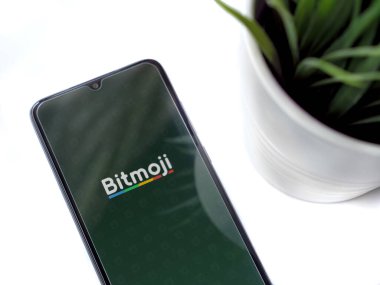 Lod, Israel - 8 Temmuz 2020: Beyaz arka planda logosu olan Botmoji uygulamalı siyah cep telefonlu modern minimalist ofis çalışma alanı. Üst görünüm yatağını kapat.