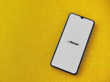 Lod, Israel - 8 Temmuz 2020: Sarı kumaş arka planda siyah bir cep telefonunun logosu olan Deezer Music Player uygulama ekranı. Üst görünüm düzlüğü kopyalama alanı ile yatıyordu.