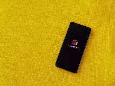 Lod, Israel - 8 Temmuz 2020: Sarı kumaş arka planda siyah bir cep telefonunun logosu olan cep telefonu uygulaması fırlatma ekranı. Üst görünüm düzlüğü kopyalama alanı ile yatıyordu.