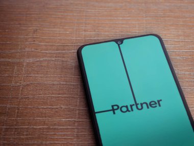 Lod, Israel - 8 Temmuz 2020: Ahşap arka planda siyah bir cep telefonunun logosu olan Partner Uygulama Fırlatma Ekranı. Üst görünüm düzlüğü kopyalama alanı ile yatıyordu.
