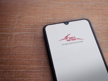 Lod, Israel - 8 Temmuz 2020: İsrail Posta uygulaması başlatma ekranı İbranice metinde logo ile ahşap arka planda siyah bir cep telefonu görüntüsü. Üst görünüm düzlüğü kopyalama alanı ile yatıyordu.