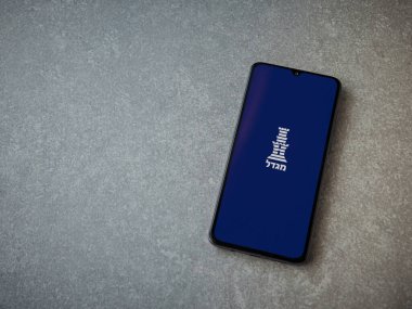 Lod, Israel - 8 Temmuz 2020: Seramik taş zemin üzerinde siyah bir cep telefonunun ekranında İbranice metinde logo bulunan Migdal uygulama başlatma ekranı. Üst görünüm düzlüğü kopyalama alanı ile yatıyordu.