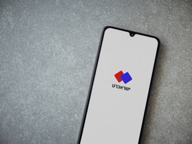 Lod, Israel - 8 Temmuz 2020: Isracard uygulaması seramik taş zemin üzerinde siyah bir cep telefonunun ekranında İbranice metinde logo bulunan bir uygulama başlatma ekranı. Üst görünüm düzlüğü kopyalama alanı ile yatıyordu.