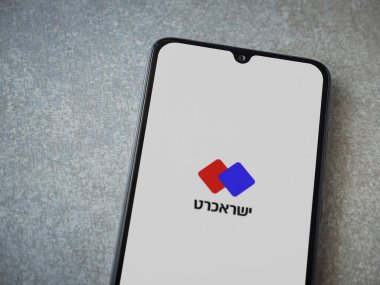 Lod, Israel - 8 Temmuz 2020: Isracard uygulaması seramik taş zemin üzerinde siyah bir cep telefonunun ekranında İbranice metinde logo bulunan bir uygulama başlatma ekranı. Üst görünüm düzlüğü kopyalama alanı ile yatıyordu.