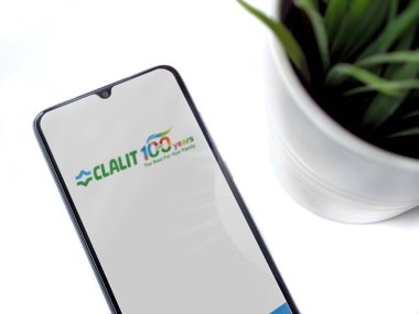 Lod, Israel - 8 Temmuz 2020: Siyah cep telefonlu modern minimalist ofis çalışma alanı ve beyaz arka planda logosu olan Clalit Sağlık Hizmetleri uygulama ekranı. Üst görünüm düzlüğü kopyalama alanı ile yatıyordu.