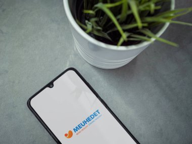 Lod, Israel - 8 Temmuz 2020: Meuhedet Sağlık Hizmetleri uygulaması logosu mermer arka planda olan siyah cep telefonlu modern minimalist ofis çalışma alanı. Üst görünüm düzlüğü kopyalama alanı ile yatıyordu.