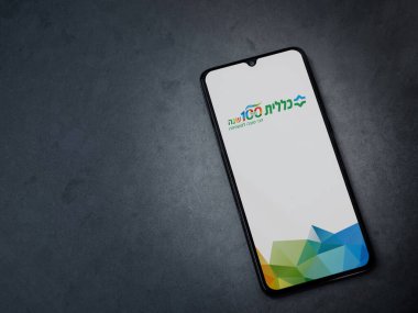 Lod, Israel - 8 Temmuz 2020: Clalit Sağlık Hizmetleri uygulaması koyu mermer taşlı arka planda siyah bir cep telefonunun logosu İbranice metin ile çalıştırma ekranı. Üst görünüm düzlüğü kopyalama alanı ile yatıyordu.