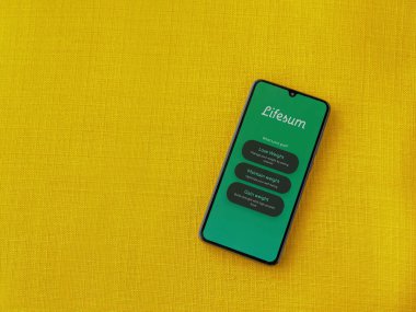 Lod, Israel - 8 Temmuz 2020: Sarı kumaş arka planda siyah bir cep telefonunun logosu olan Lifesum uygulaması fırlatma ekranı. Üst görünüm düzlüğü kopyalama alanı ile yatıyordu.