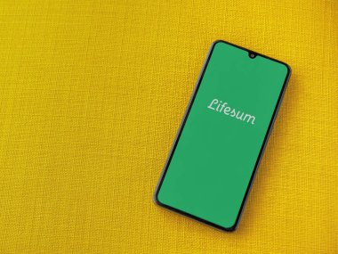 Lod, Israel - 8 Temmuz 2020: Sarı kumaş arka planda siyah bir cep telefonunun logosu olan Lifesum uygulaması fırlatma ekranı. Üst görünüm düzlüğü kopyalama alanı ile yatıyordu.