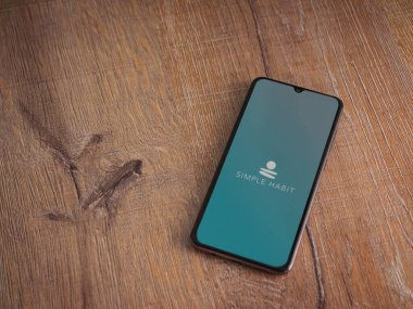 Lod, Israel - 8 Temmuz 2020: Ahşap arka planda siyah bir cep telefonunun logosu olan Basit Alışkanlık uygulaması başlatma ekranı. Üst görünüm düzlüğü kopyalama alanı ile yatıyordu.