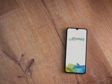 Lod, Israel - 8 Temmuz 2020: Clalit Sağlık Hizmetleri uygulama ekranı İbranice metinlerle siyah bir cep telefonunun ahşap arka planda sergilenmesi ile başlatıldı. Üst görünüm düzlüğü kopyalama alanı ile yatıyordu.