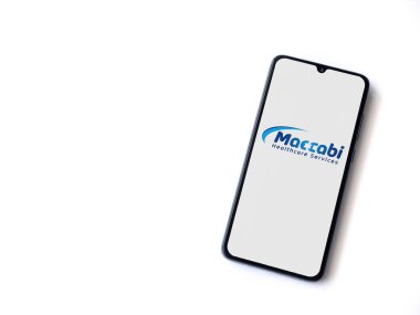 Lod, Israel - 8 Temmuz 2020: Maccbi Sağlık Hizmetleri uygulaması beyaz arkaplanda izole edilmiş siyah bir cep telefonunun logosu ile fırlatma ekranı. Üst görünüm düzlüğü kopyalama alanı ile yatıyordu.