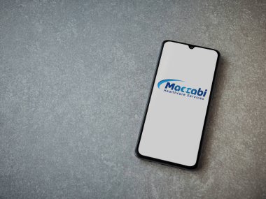 Lod, Israel - 8 Temmuz 2020: Maccbi Sağlık Hizmetleri uygulaması seramik taş zemin üzerinde siyah bir cep telefonunun logosu olan fırlatma ekranı. Üst görünüm düzlüğü kopyalama alanı ile yatıyordu.