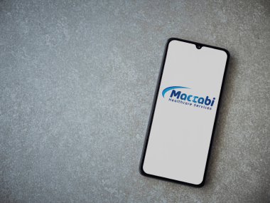 Lod, Israel - 8 Temmuz 2020: Maccbi Sağlık Hizmetleri uygulaması seramik taş zemin üzerinde siyah bir cep telefonunun logosu olan fırlatma ekranı. Üst görünüm düzlüğü kopyalama alanı ile yatıyordu.