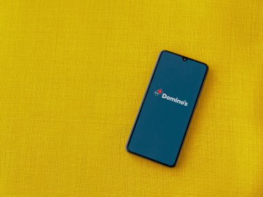Lod, Israel - 8 Temmuz 2020: Domino 's Pizza Israel uygulama ekranı üzerinde sarı kumaş arka planda siyah bir cep telefonunun logosu var. Üst görünüm düzlüğü kopyalama alanı ile yatıyordu.