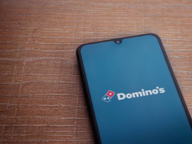 Lod, Israel - 8 Temmuz 2020: Domino 'nun Pizza Israel uygulaması, tahta arka planda siyah bir cep telefonunun logosu ile başlatıldı. Üst görünüm düzlüğü kopyalama alanı ile yatıyordu.