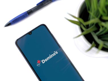 Lod, Israel - 8 Temmuz 2020: Domino 'nun Pizza Israel uygulamasının beyaz arka planda logosu olan siyah cep telefonlu modern minimalist ofis çalışma alanı. Üst görünüm yatağını kapat.