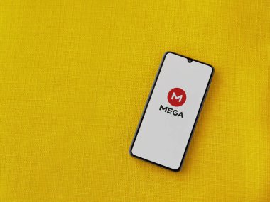 Lod, Israel - 8 Temmuz 2020: MeGA uygulama başlatma ekranı üzerinde sarı kumaş arka planda siyah bir cep telefonunun logosu var. Üst görünüm düzlüğü kopyalama alanı ile yatıyordu.