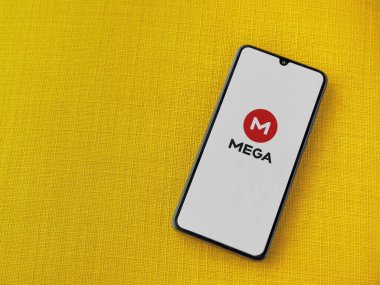 Lod, Israel - 8 Temmuz 2020: MeGA uygulama başlatma ekranı üzerinde sarı kumaş arka planda siyah bir cep telefonunun logosu var. Üst görünüm düzlüğü kopyalama alanı ile yatıyordu.