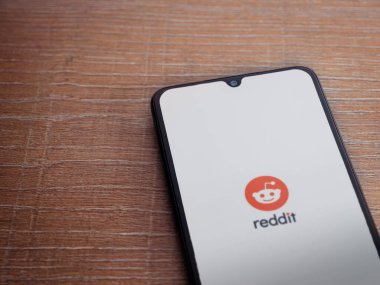 Lod, Israel - 8 Temmuz 2020: Ahşap arka planda siyah bir cep telefonunun logosu olan Reddit uygulaması fırlatma ekranı. Üst görünüm düzlüğü kopyalama alanı ile yatıyordu.