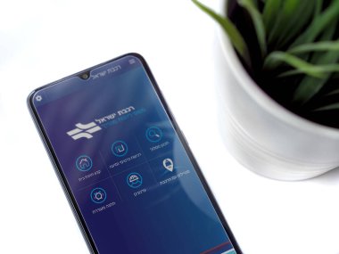 Lod, Israel - 8 Temmuz 2020: İsrail Demiryolları uygulamalı siyah cep telefonlu modern minimalist ofis çalışma alanı beyaz arkaplan üzerine İbranice metin ile logo fırlatma ekranı. Üst görünüm düzlüğü kopyalama alanı ile yatıyordu.