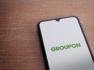 Lod, Israel - 8 Temmuz 2020: Groupon uygulama ekranında siyah bir cep telefonunun ahşap arka planda logosu var. Üst görünüm düzlüğü kopyalama alanı ile yatıyordu.