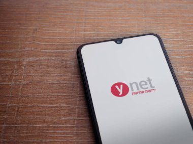 Lod, Israel - 8 Temmuz 2020: ynet uygulama başlatma ekranı üzerinde siyah bir cep telefonunun logosu olan ahşap arka planda. Üst görünüm düzlüğü kopyalama alanı ile yatıyordu.