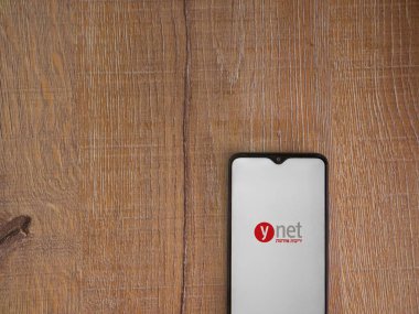 Lod, Israel - 8 Temmuz 2020: ynet uygulama başlatma ekranı üzerinde siyah bir cep telefonunun logosu olan ahşap arka planda. Üst görünüm düzlüğü kopyalama alanı ile yatıyordu.