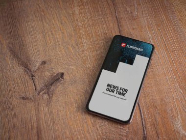 Lod, Israel - 8 Temmuz 2020: Flipboard uygulama başlatma ekranı üzerinde siyah bir cep telefonunun logosu olan ahşap arka planda. Üst görünüm düzlüğü kopyalama alanı ile yatıyordu.