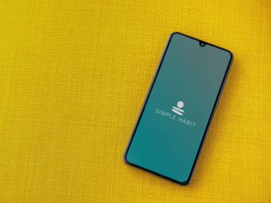 Lod, Israel - 8 Temmuz 2020: Sarı kumaş arka planda siyah bir cep telefonunun logosu olan Basit Alışkanlık uygulaması başlatma ekranı. Üst görünüm düzlüğü kopyalama alanı ile yatıyordu.