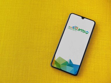 Lod, Israel - 8 Temmuz 2020: Clalit Sağlık Hizmetleri uygulaması sarı kumaş arka planda siyah bir cep telefonunun logosu İbranice metin ile çalıştırma ekranı. Üst görünüm düzlüğü kopyalama alanı ile yatıyordu.
