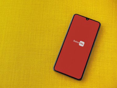 Lod, Israel - 8 Temmuz 2020: BetterMe uygulama ekranı üzerinde sarı kumaş arka planda siyah bir cep telefonunun logosu var. Üst görünüm düzlüğü kopyalama alanı ile yatıyordu.