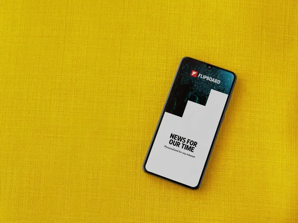 Lod, Israel - 8 Temmuz 2020: Sarı kumaş arka planda siyah bir cep telefonunun logosu olan Flipboard uygulama başlatma ekranı. Üst görünüm düzlüğü kopyalama alanı ile yatıyordu.