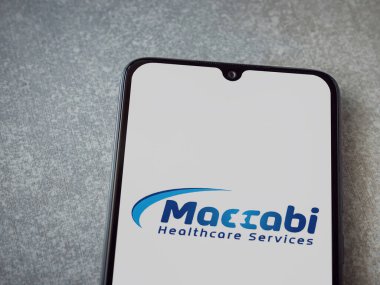 Lod, Israel - 8 Temmuz 2020: Maccbi Sağlık Hizmetleri uygulaması seramik taş zemin üzerinde siyah bir cep telefonunun logosu olan fırlatma ekranı. Üst görünüm düzlüğü kopyalama alanı ile yatıyordu.