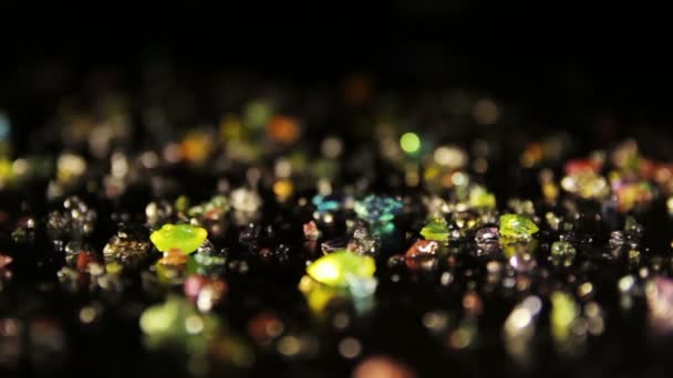 Diamantförmige farbige Kristalle, die auf einem schwarzen Tisch verstreut sind. Schwenk geschossen. — Stockvideo