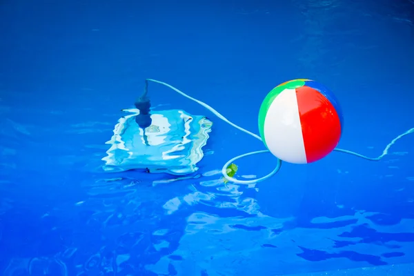 Colorful beach ball floating in pool and next to him underwater a cleaning robot