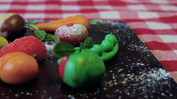 Marzipan fruits are placed on a wooden brown board on a table — Stock Video