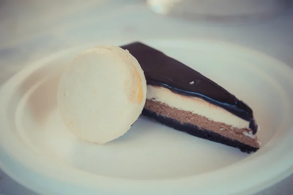 Piece of chocolate-vanilla mousse cake with Glsaz of chocolate and white macaroon on a white plate. — Stock Photo, Image