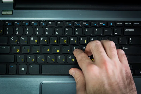 Man typing on a keyboard with letters in Hebrew and English