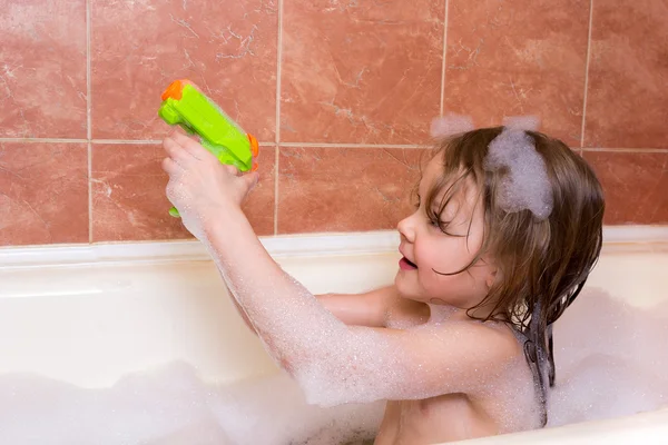 Маленькая девочка играет с водяным пистолетом в ванне с пеной — стоковое фото
